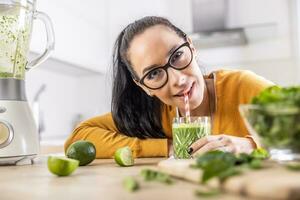 A funny young woman drinks a green smoothie that she made herself. photo