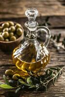 Transparent, golden olive oil is designed with olives in wooden bowl and leaves of olives photo