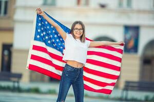 Happy young american school girl holding and waving in the city with USA flag photo