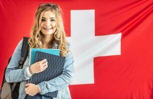 Student in braces smiles holding study material in from of flag of Switzerland photo