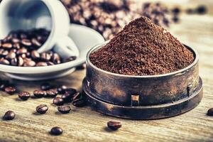 Freshly grinded coffee in rustic grinder with cup and beans in the background. Everything placed on wooden desk photo