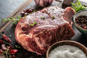 Raw beef steak on wooden cutting board with salt spices chili peppers thyme and rosemary photo