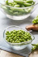 Fresh green pea seeds in bowl on kitchen table photo