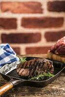 Grilled beef steak in grill pan with herbs rosemary on wooden table photo