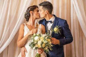 Newlyweds that just got married are having their first kiss with champagne in their hands photo