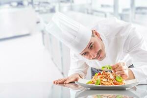 Chef in restaurant kitchen prepares and decorates meal with hands. Cook preparing spaghetti bolognese photo