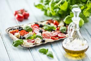 Caprese salad with mozzarella cheese ripe tomatoes olives and basil leaves. Italian or mediterranean healthy meal photo