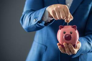 ahorro dinero. hombre de negocios participación rosado cerdito y poniendo moneda dentro cerdito banco. foto