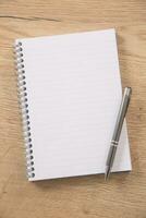 White lined notepad with a metal ring wire binding and a silver pen opened on a wooden surface photo