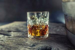 vaso con whisky Ron brandy o Borbón en un antiguo mesa cerca un de madera barril foto