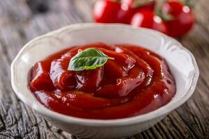Ketchup or tomato sauce in white bowl and cherry tomatoes on wooden table. photo