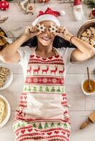 A cheerful cook in a Christmas apron lies on the ground and covers her eyes with cakes, surrounded by traditional holiday dishes and cakes photo