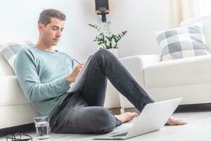 Man working from home writes down on paper while sitting on the floor photo