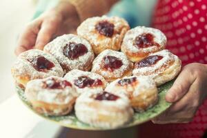 Plate full of jam-filled donuts with sugar coating held in the hands of an older woman photo