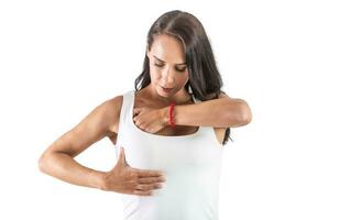 joven mujer checando su senos vistiendo un blanco parte superior y haciendo autoexamen a evitar cáncer. aislado antecedentes foto