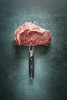 Raw beef steak with fork on dark concrete background photo