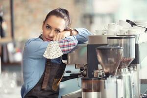 Bored waitress leans against the coffee machine with no job to do, holding face mask in her hand photo