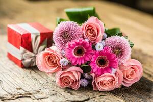 Beautiful bouquet of flowers with red gift on wooden table. photo