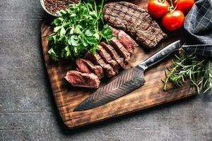 Slices of juicy grilled beef steak with knife on a butcher plate photo