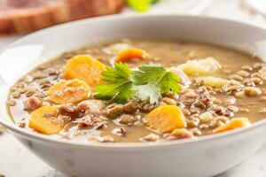 Lentil soup with pieces of smoked pork neck, carrots, potatoes and coriander photo