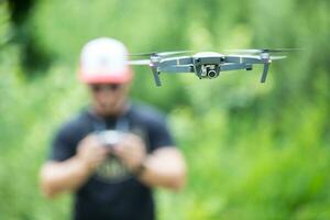 Young man holding remote controller and flying with drone in the park photo