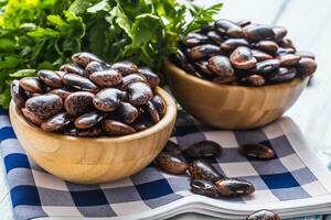 Uncooked beans in wooden bowles  with parsley herbs on kitchen table photo