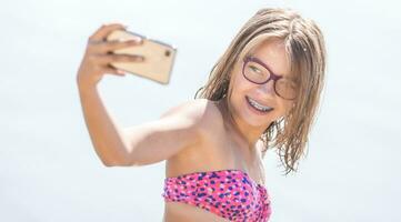 Happy young girl with dental braces making selfhie on beach in summer hot day photo