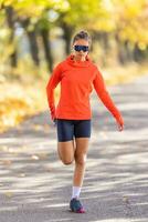 joven hembra atleta en ropa de deporte es calentamiento arriba antes de corriendo en el otoño parque foto