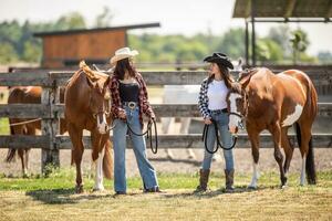 dos equitación muchachas discutir caballos en un rancho mientras en pie siguiente a ellos foto