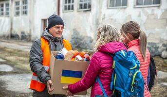 Vysne Nemecke, Slovakia. March 30. 2022. Volunteer in orange west gives a box of food donation to fleeing refugees from Ukraine photo