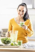 Smiling woman holding a glass of spinach green smoothie. photo