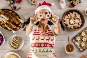 A cheerful cook in a Christmas apron lies on the ground and covers her eyes with cakes, surrounded by traditional holiday dishes and cakes photo