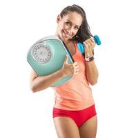 Happy fit woman holds dumbbell in one hand and an old school scale in the second hand photo