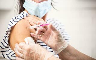 detalle de médico poniendo covid-19 vacuna mediante inyección dentro el brazo de un hembra vistiendo cara máscara foto