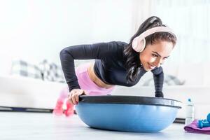 Beautiful fit woman does workout at home with headphones on, doing pushups on a balance ball photo