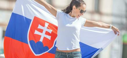 hermosa joven mujer sostiene un bandera de Eslovaquia exteriores en un soleado día, vistiendo Gafas de sol foto