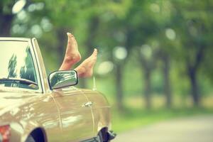 Bare feet sticking out of a cabrio vintage car parked in the nature photo