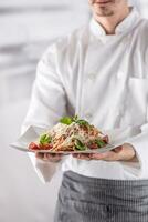 Chef in restaurant kitchen holding plate with italian meal spaghetti bolognese photo