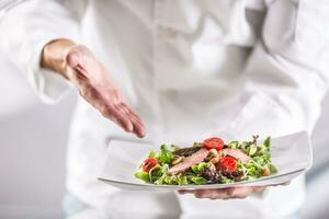 Chef in the kitchen of the hotel or restaurant showing on the food just before serving photo