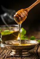 Honey. Honey and honey dipper on rustic oak table. Hot herb tea in the background photo