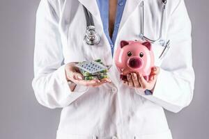 Doctor woman hands holding pills and piggy bank photo