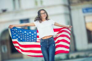 Happy young american school girl holding and waving in the city with USA flag photo