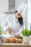 Happy, focusing, professional female chef runs knife through fresh fillet of fish with fresh herbs on the side photo