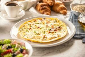 Fresh omelette served on a plate sprinkled with chopped chilli and cilantro, served along with assortment of breakfast food and coffee photo