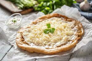 Closeup of a hungarian baked langos served with loevly cream, cheese, garlic and fresh green onion photo