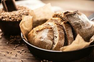 Lovely crunchy yeast bread slices served on the baking paper in the alloy rustic pan on the wooden table with whole wheat grains in the background photo