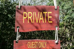 firmar diciendo privado y invitados solamente en un de madera rústico tablero escrito en amarillo permitiendo acceso solamente a el invitados de un tropical turismo recurso foto