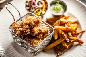 Fried chicken nuggets in metal basket served with french fries on a white plate photo