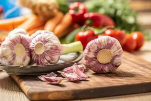 Five heads of garlic on a cutting board with various vegetables in the background photo