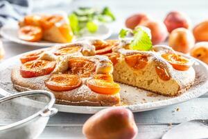 Apricot pie on a white plate, apricots, mint and powdered sugar on the kitchen table photo